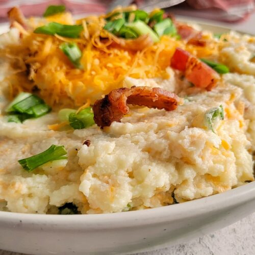 cauliflower mash in a bowl topped with bacon, green onions and cheddar cheese