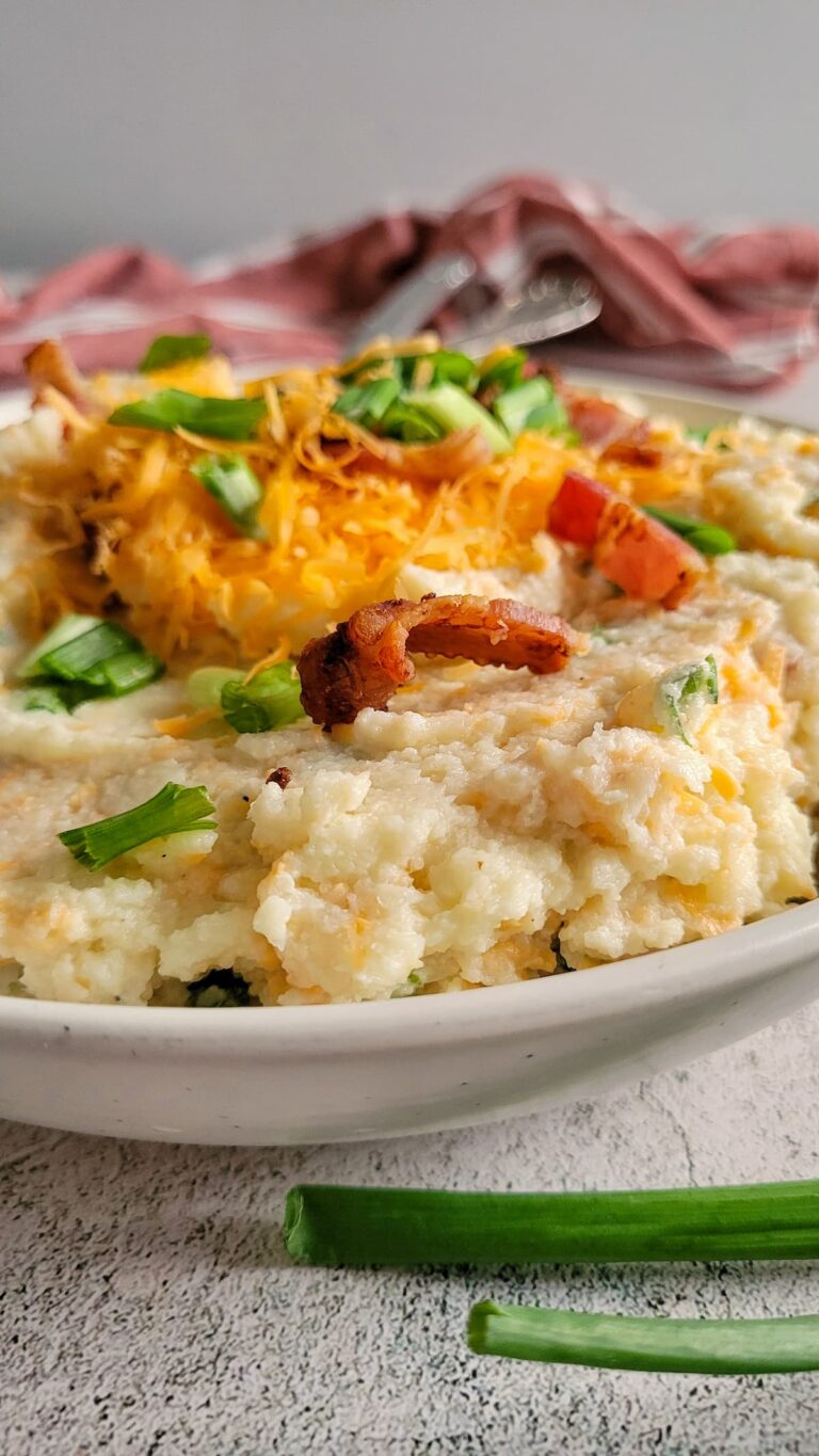 cauliflower mash in a bowl topped with bacon, green onions and cheddar cheese