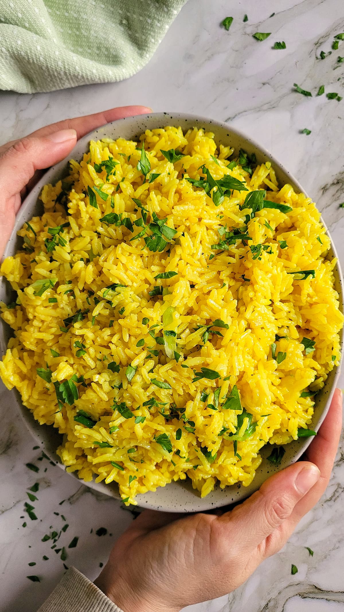 hands holding a bowl of turmeric rice garnished with parsley and green onions