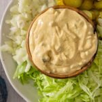 mac sauce in a bowl on a plate with sliced pickles, shredded lettuce and diced white onions