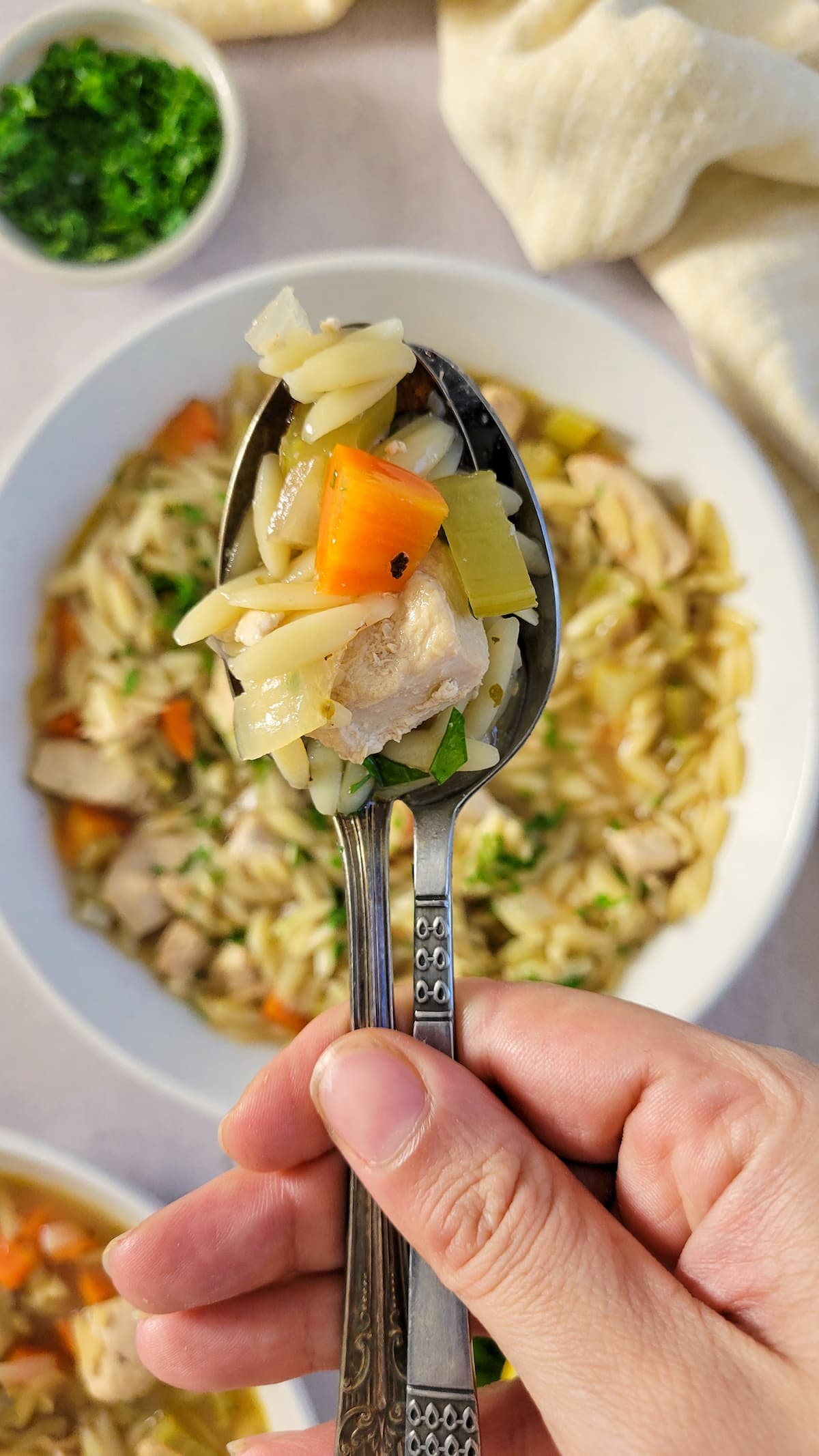 hand holding a spoonful of greek chicken soup with lemon and orzo over a bowl of the rest of it