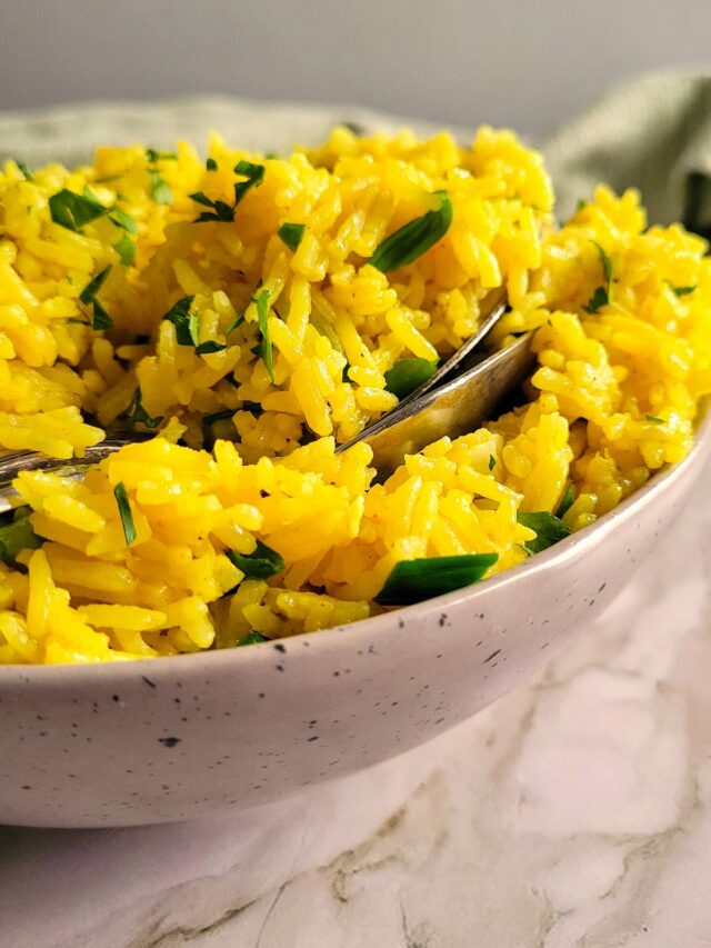 bowl of yellow rice with parsley and two spoons