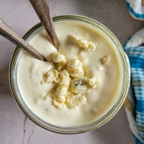 blue cheese dressing in a jar topped with blue cheese crumbles, two spoons in the jar