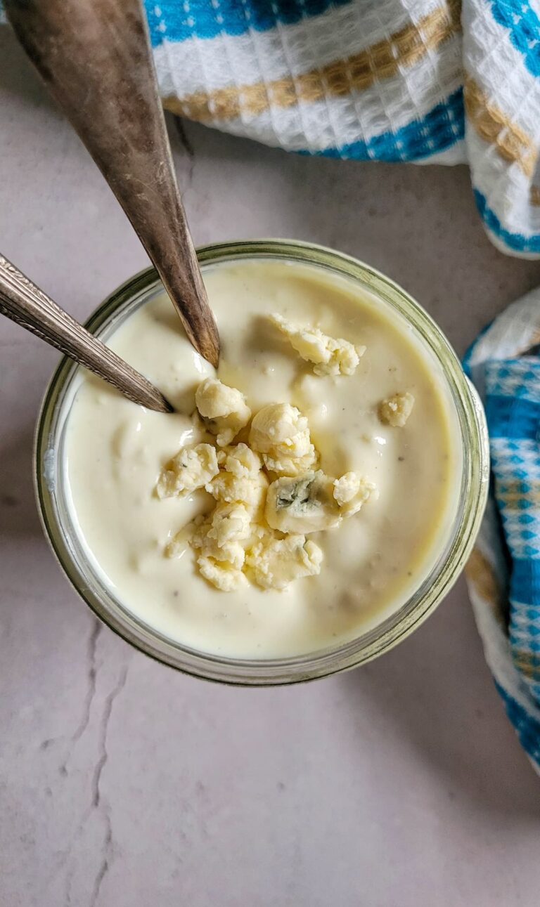 blue cheese dressing in a jar topped with blue cheese crumbles, two spoons in the jar