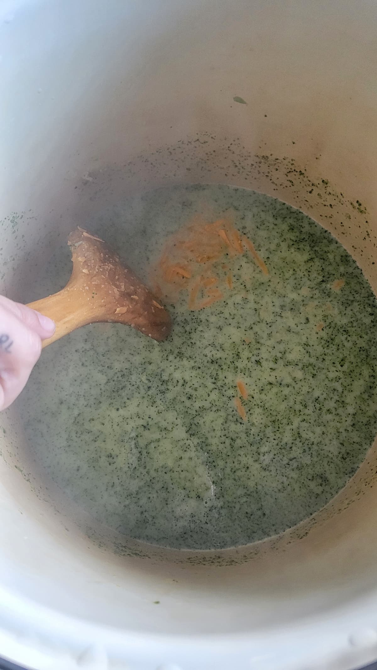 hand with a wooden spatula stirring shredded cheddar cheese into a pot of broccoli soup