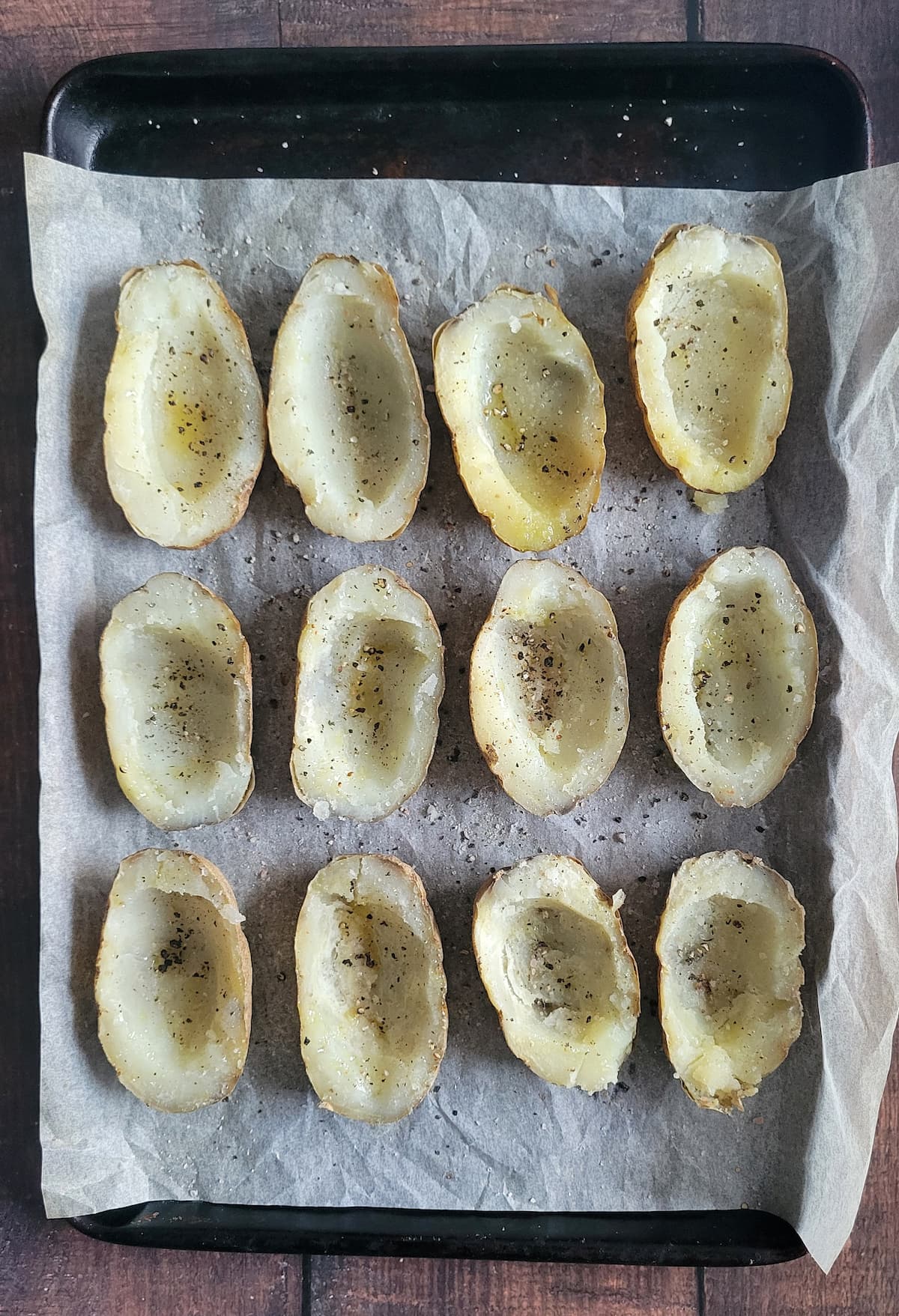 hollowed potato halves with salt, pepper and oil on a parchment lined baking sheet