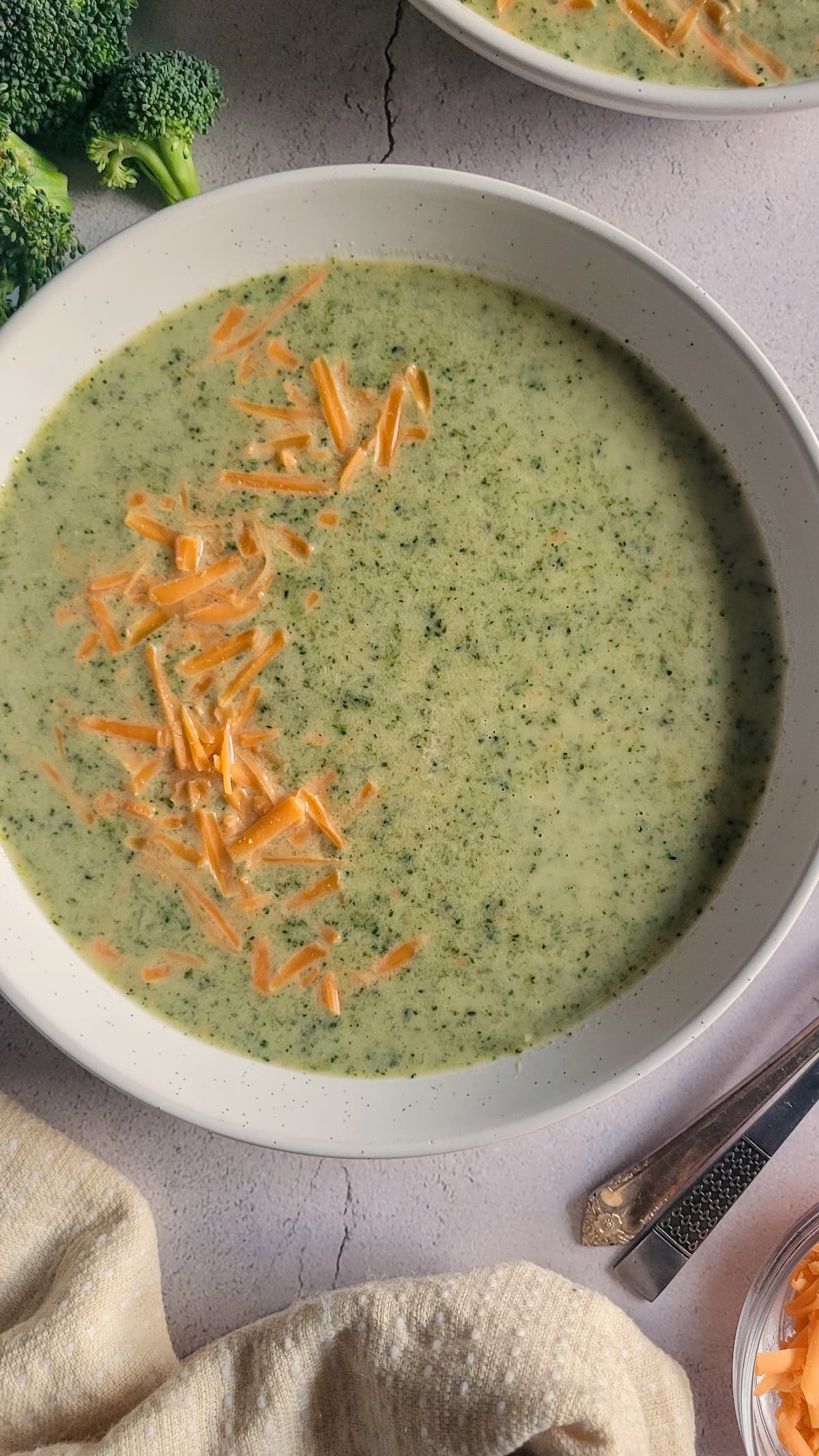 bowl of broccoli cheddar soup next to some broccoli florets