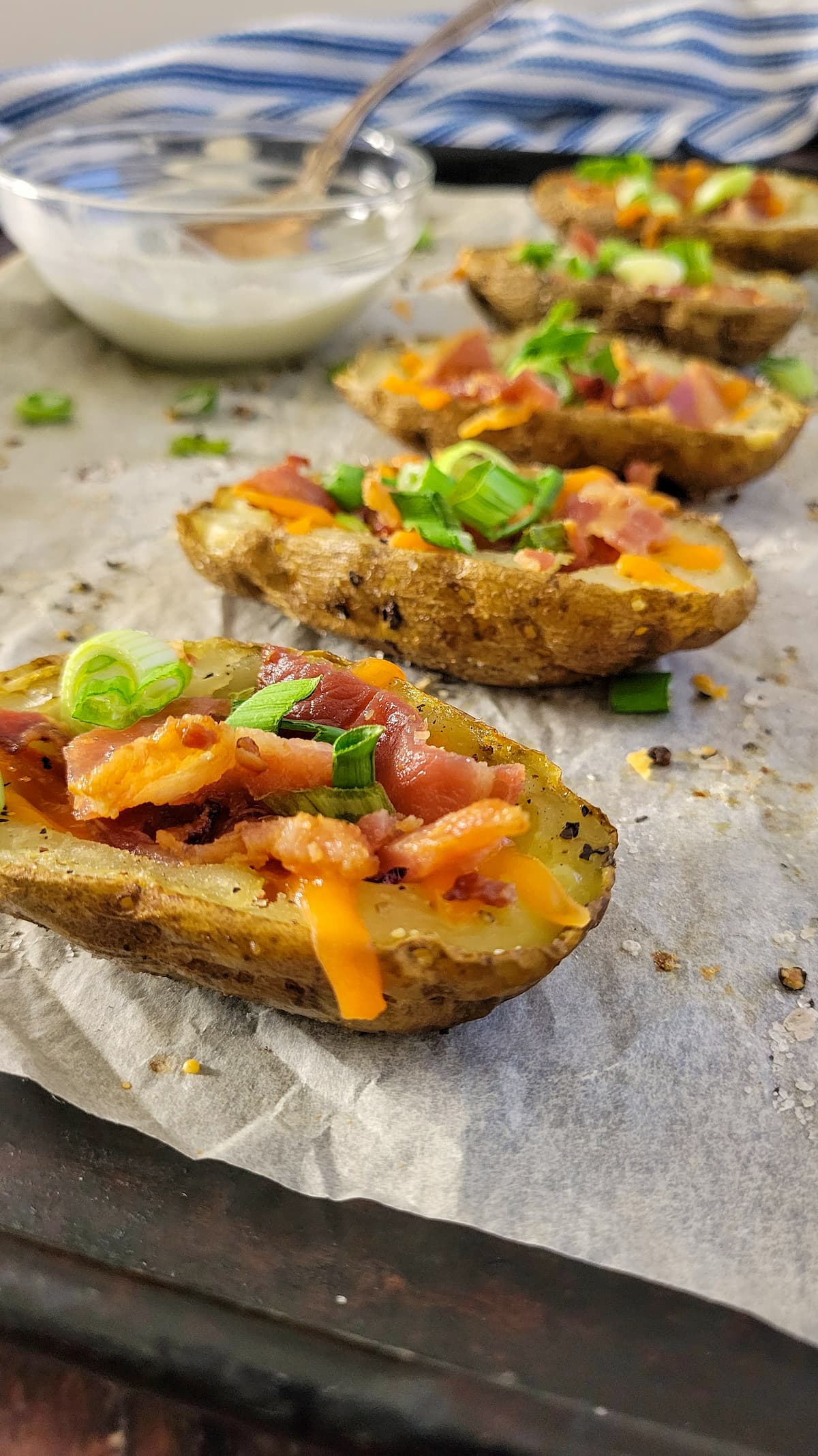 loaded potato skins on a parchment lined baking sheet with a bowl of sour cream in the background