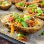 potato skins stuffed with cheddar cheese, bacon and green onions on a parchment lined baking sheet