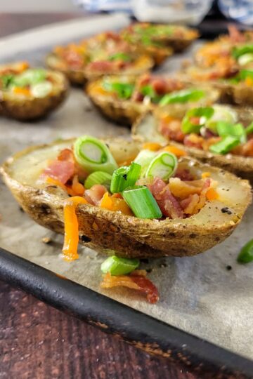 potato skins stuffed with cheddar cheese, bacon and green onions on a parchment lined baking sheet