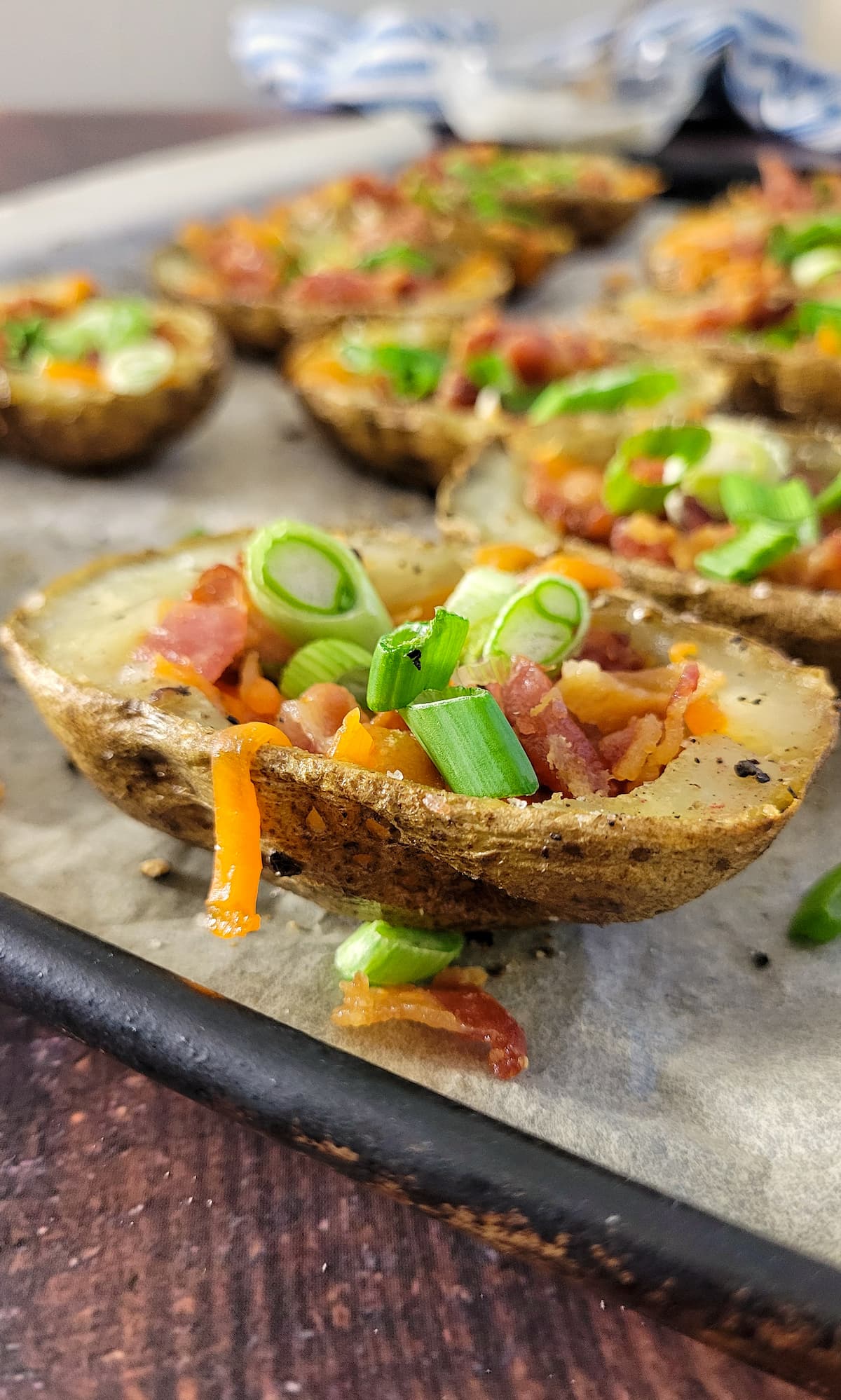 potato skins stuffed with cheddar cheese, bacon and green onions on a parchment lined baking sheet