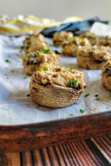 crab filled mushrooms on a parchment lined baking sheet garnished with fresh chopped parsley
