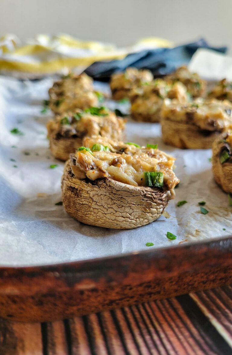 crab filled mushrooms on a parchment lined baking sheet garnished with fresh chopped parsley