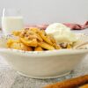 apple crisp in a bowl with ice cream, glass of milk in the background, cinnamon sticks in the front
