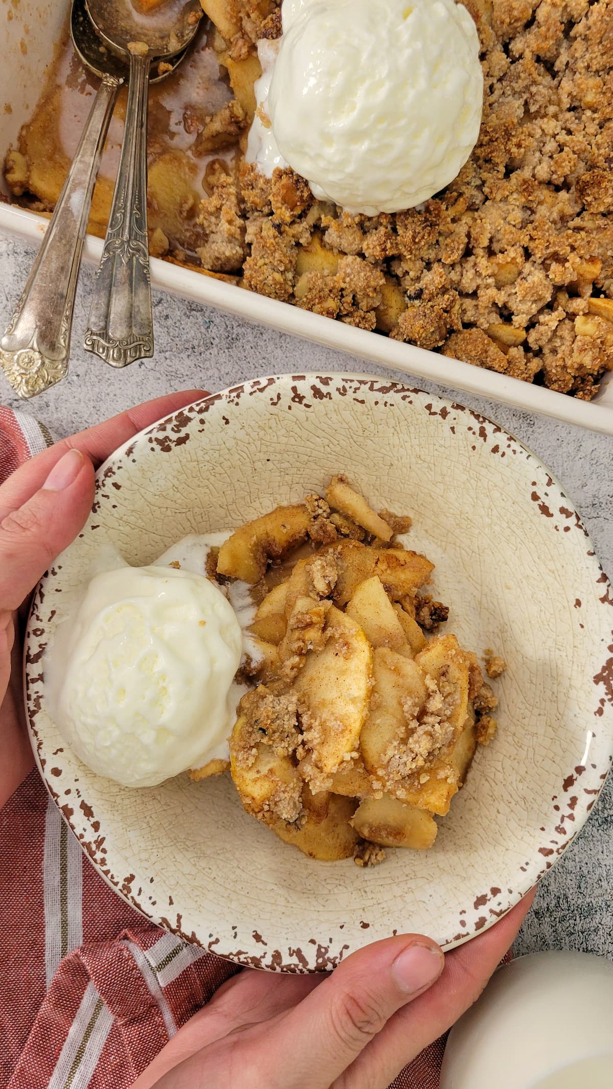 hands holding a bowl of apple crisp with ice cream, pan with more in the background