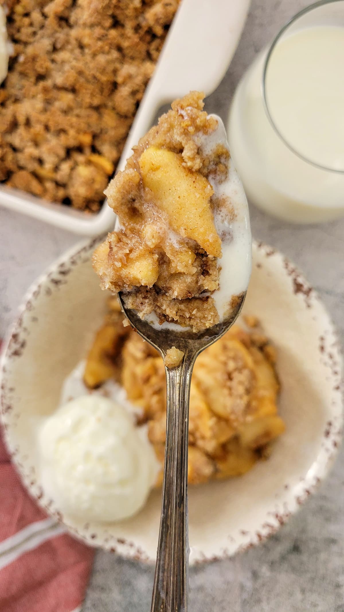 apple crisp on a spoon over a bowl with some and ice cream and a pan with more