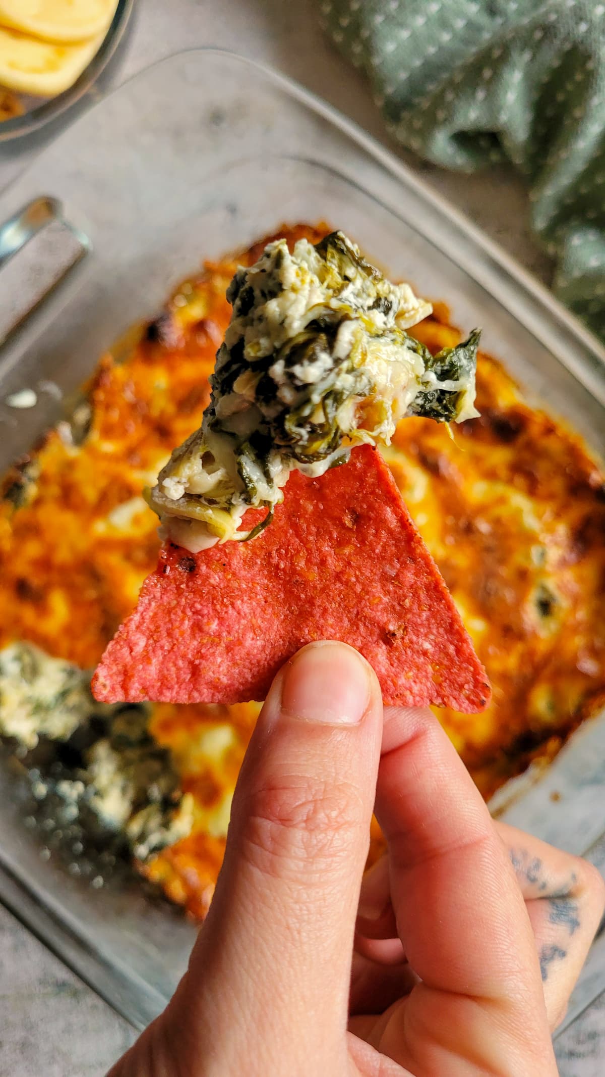 spinach and artichoke dip on a red tortilla chip above a glass baking dish with the rest of it