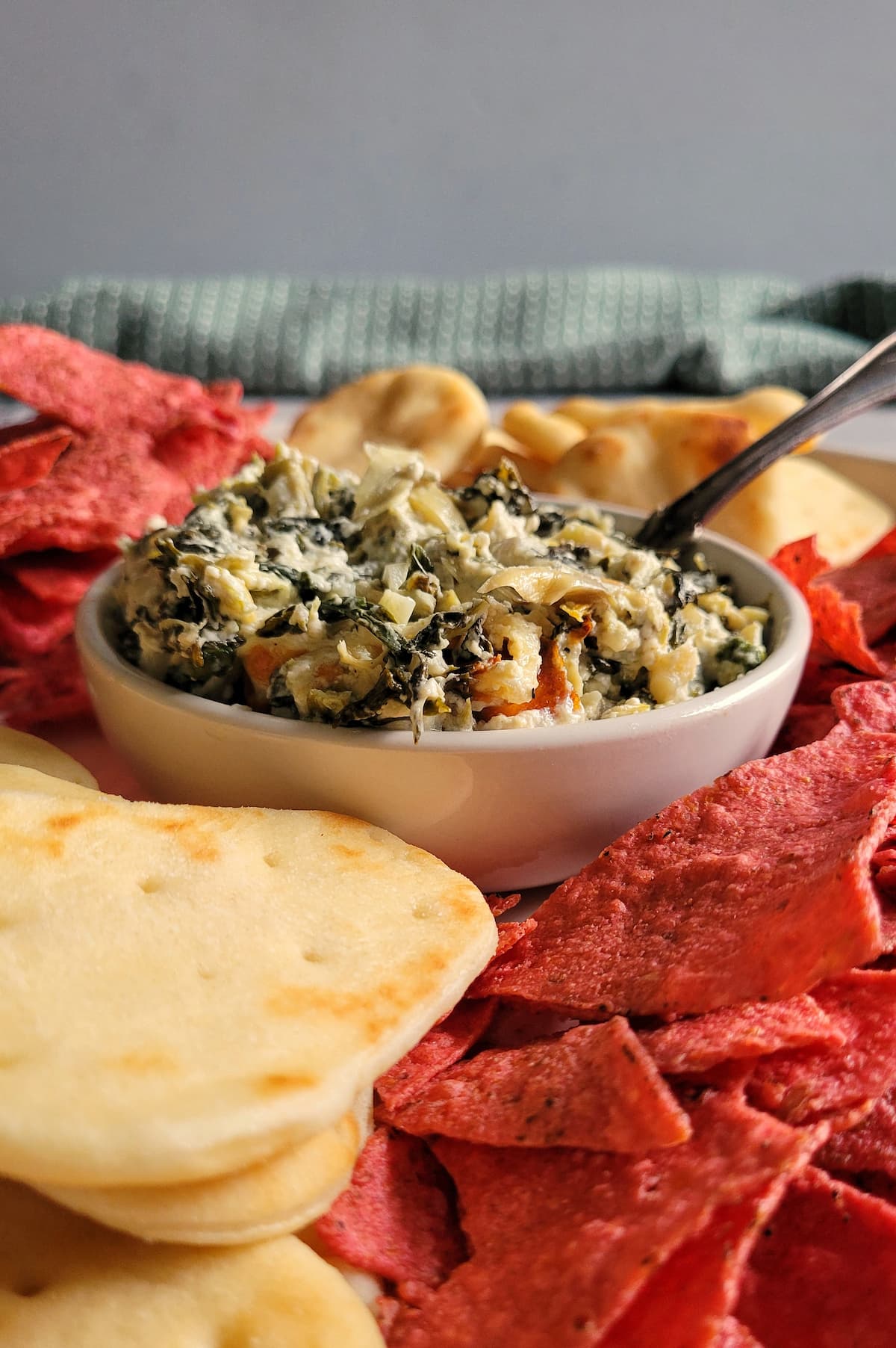 spinach and artichoke dip in a bowl surrounded by red tortilla chips and pita