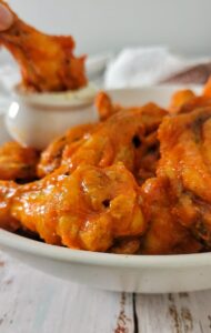 bowl of hot chicken wings, one dipping into a white sauce in the background