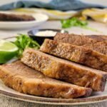 sliced brisket on a plate with lime, white sauce and greens