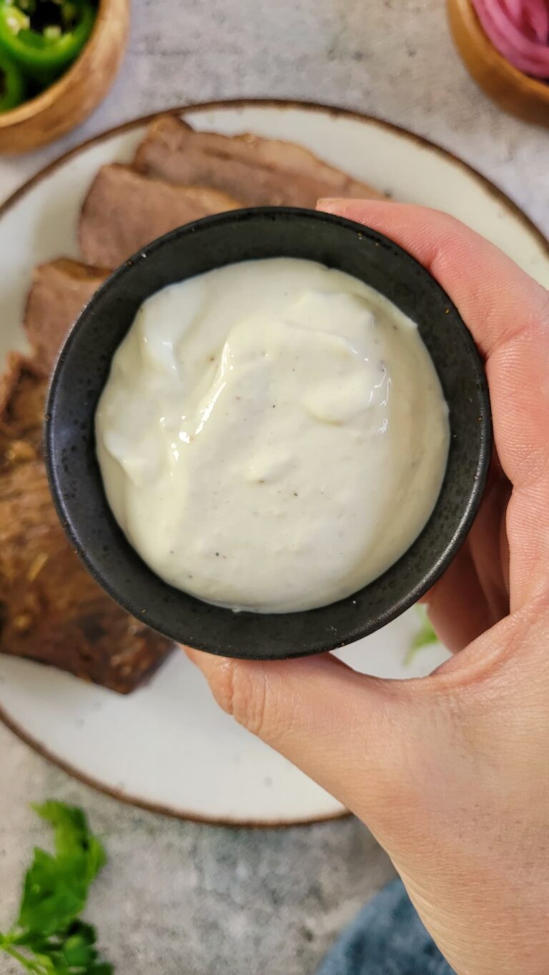 creamy white sauce in a black ramekin over a plate of sliced brisket