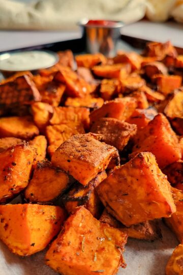 tray of roasted cubed sweet potatoes, ketchup and white sauce in the background