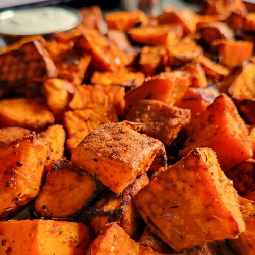 tray of roasted cubed sweet potatoes, ketchup and white sauce in the background