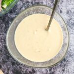 bowl of creamy white sauce with a spoon in it, salad in the background