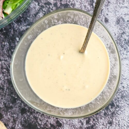bowl of creamy white sauce with a spoon in it, salad in the background