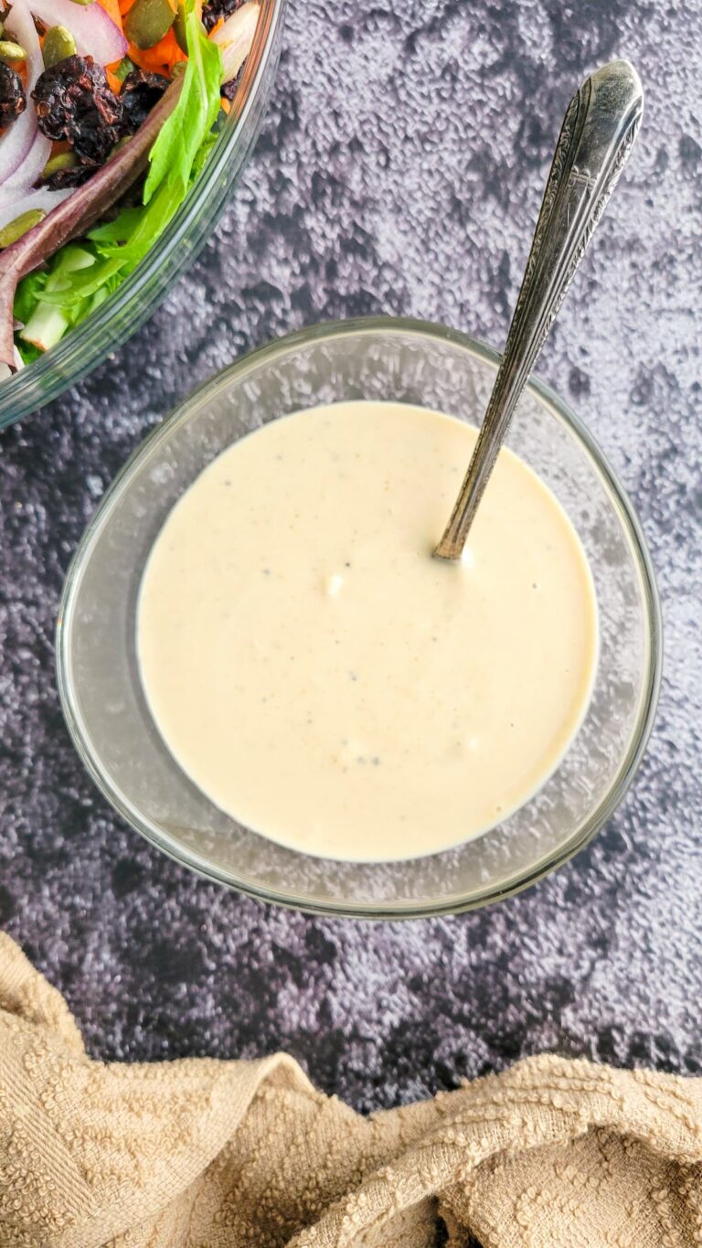 bowl of creamy white sauce with a spoon in it, salad in the background