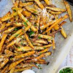 parm fries on a parchment lined baking sheet with sauces and fresh chopped parsley