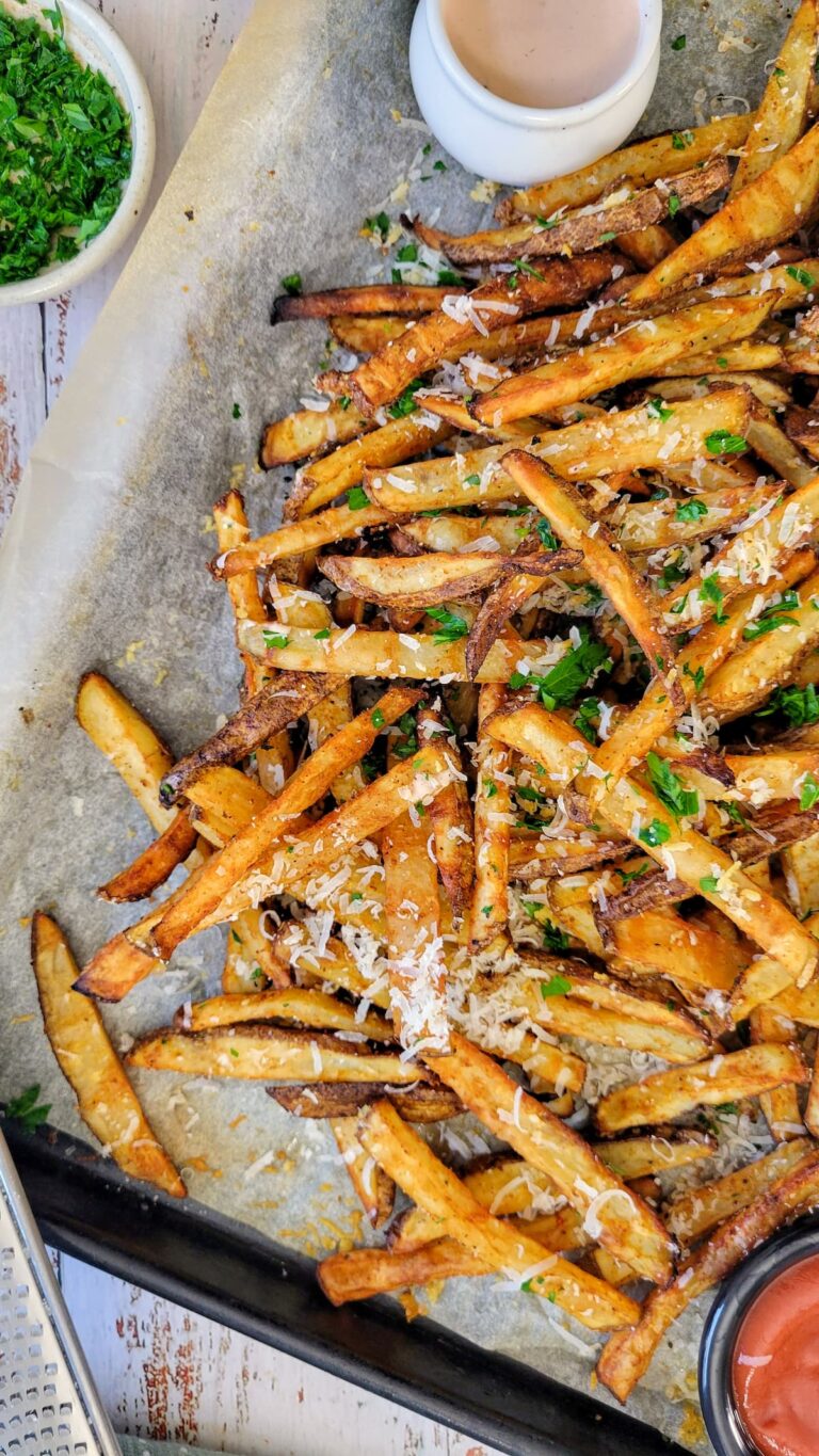 parmesan fries with chopped parsley on a parchment lined baking sheet with sauces