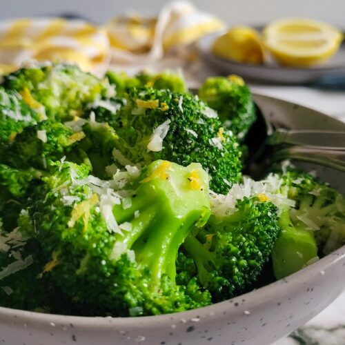 cooked broccoli florets in a bowl with lemon zest and parmesan cheese
