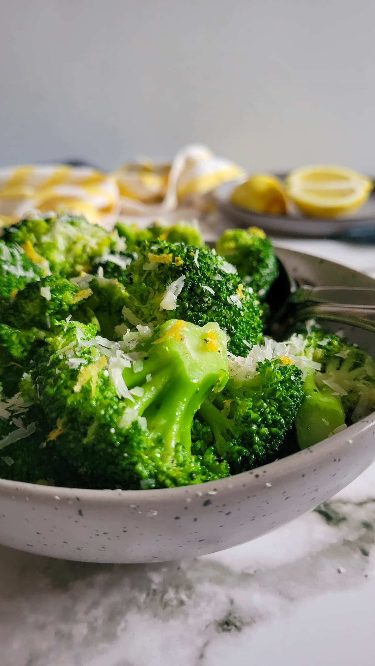 cooked broccoli florets in a bowl with lemon zest and parmesan cheese