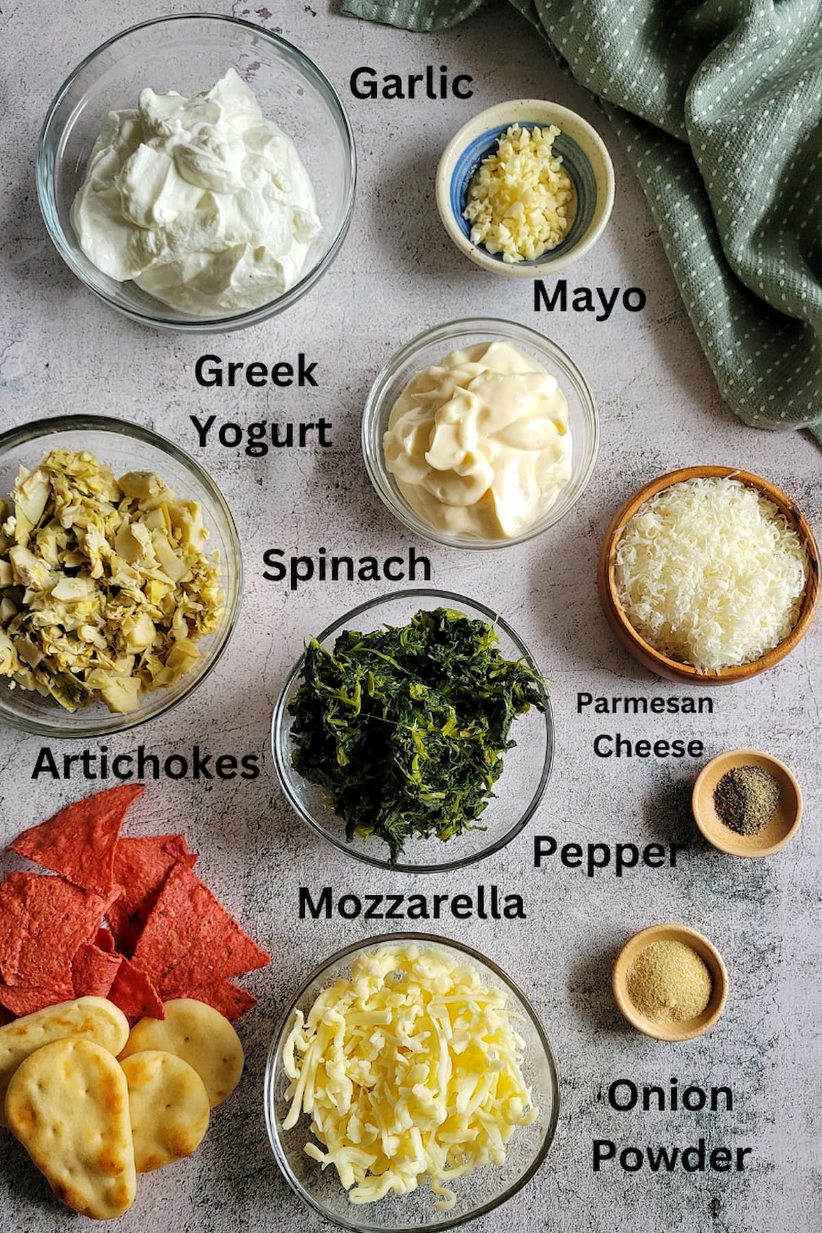 ingredients for spinach artichoke dip recipe - garlic, mayo, greek yogurt, spinach, artichokes, mozzarella, parmesan cheese, pepper, onion powder, tortilla chips, pita bread
