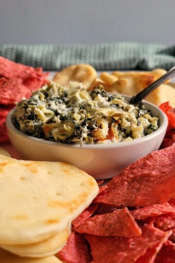 spinach and artichoke dip in a bowl surrounded by red tortilla chips and pita