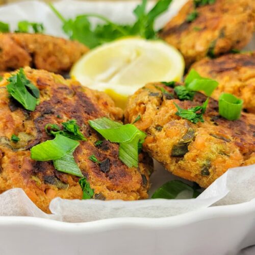 salmon cakes on a lined plate with a half a lemon, garnished with fresh chopped parsley and green onions