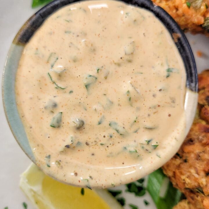 orange remoulade in a ramekin on a plate with a lemon wedge and salmon cakes