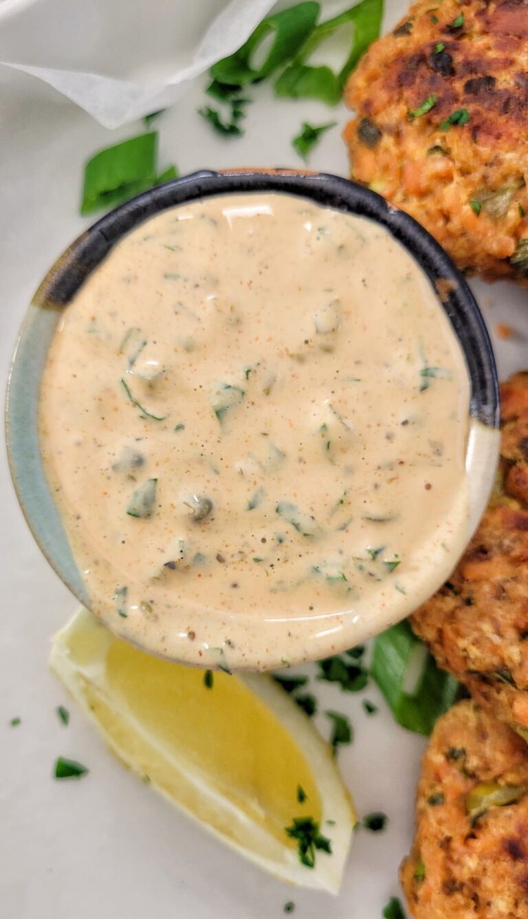orange remoulade in a ramekin on a plate with a lemon wedge and salmon cakes