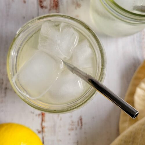 apple cider vinegar lemonade with ice and a straw, lemons in the background