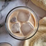 two glasses of baileys on the rocks next to a bottle of homemade baileys
