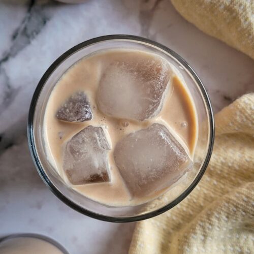 two glasses of baileys on the rocks next to a bottle of homemade baileys