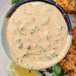 orange remoulade in a ramekin on a plate with a lemon wedge and salmon cakes