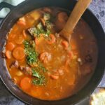 pot of irish beef stew with carrots and fresh chopped parsley, wooden spoon in the pot