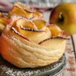 2 puff pastry apple roses in a muffin tin, whole apple in the background