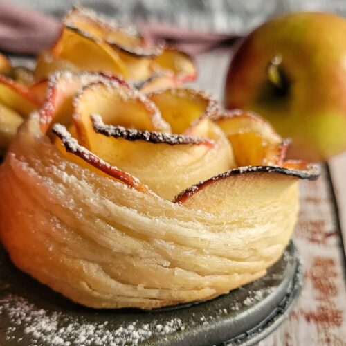 2 puff pastry apple roses in a muffin tin, whole apple in the background