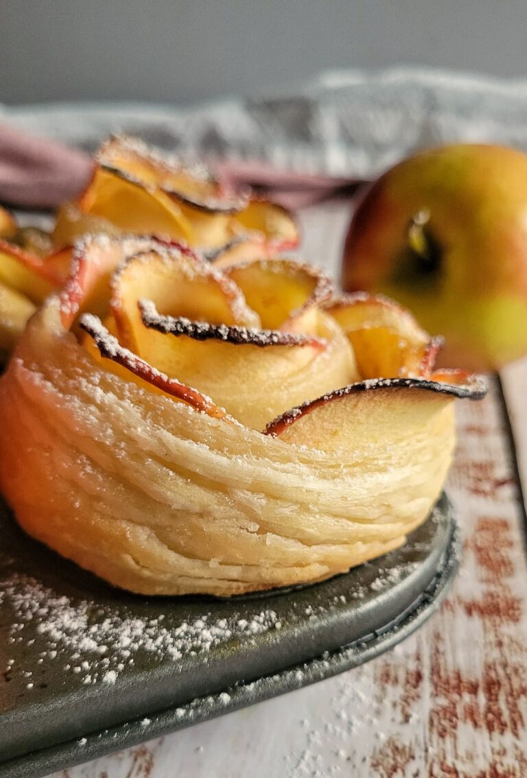 2 puff pastry apple roses in a muffin tin, whole apple in the background