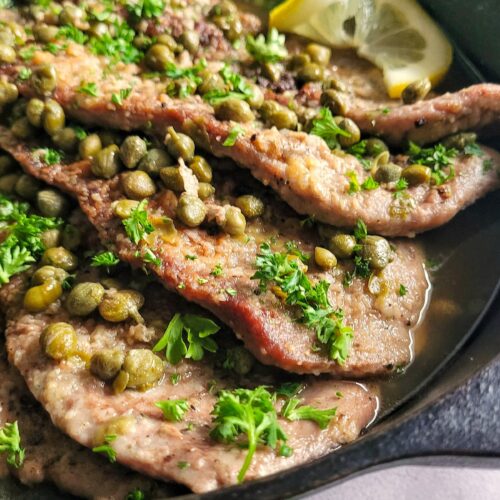 side view of veal scallopini with capers, parsley and lemon in a cast iron skillet