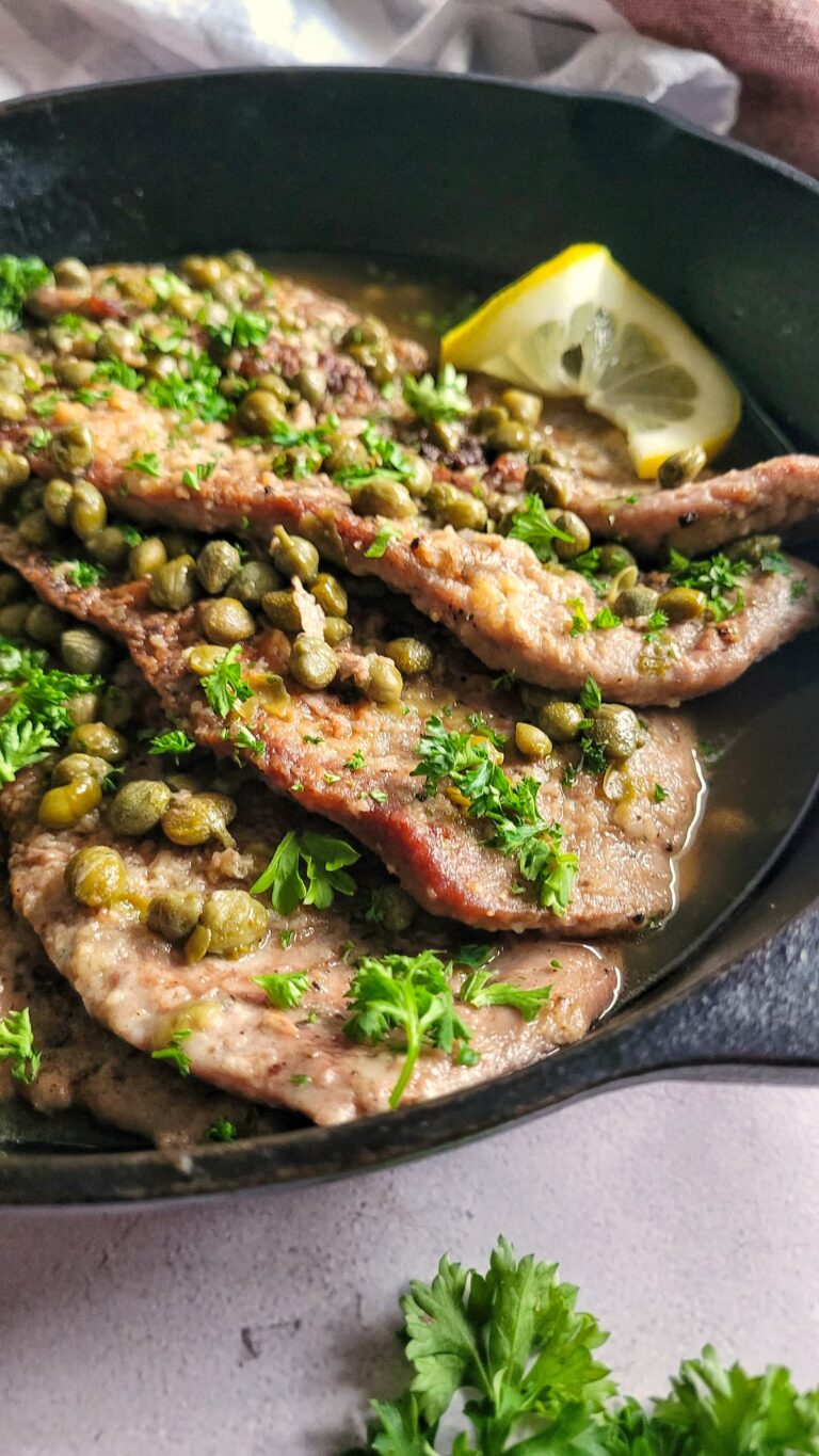 side view of veal scallopini with capers, parsley, and lemon in a cast iron skillet.