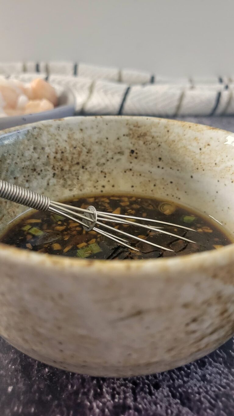 whisk in a bowl of black sauce, bowl of dumplings in the background